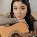 Portrait of a woman holding an acoustic guitar indoors with a thoughtful expression.