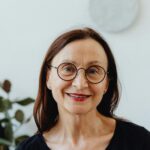 Portrait of a smiling senior woman wearing glasses against a bright indoor background.